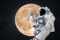 Space man astronaut greets and waves his hand in space on a background of amazing full moon. Space mission wallpaper, concept.