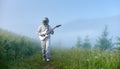 Spaceman in space suit with a guitar is walking on a beautiful green mountain meadow in foggy morning