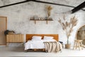 Spacious airy white industrial loft bedroom with bed, mirror and pampas grass decoration