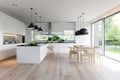 Spacious bright monochrome kitchen interior in a modern cottage. White plain facades, kitchen island, dining area Royalty Free Stock Photo