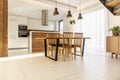 Spacious, open kitchen and dining room with wooden table and chairs, large window, white cupboards and tiles on the floor. Real p Royalty Free Stock Photo