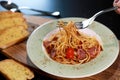 Spaghetti bacon with fork in hand and tomato in the green and white color plate and Garlic bread on wooden table background. Foods