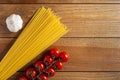 Spaghetti, cherry tomatoes and head of garlic on a brown wooden table. Tomatoes to the right of spaghetti, garlic to the left. Top