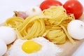 Spaghetti, eggs, onion, garlic and tomato on wooden plate