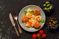 Spaghetti with meatballs in tomato sauce served in a gray plate, capers, olives, tomatoes. Black concrete background, top view. Royalty Free Stock Photo