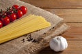 Spaghetti, pepper and cherry tomatoes on burlap. Near bulb of garlic on a brown wooden table. Tomatoes to the left of spaghetti,