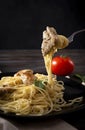 Spaghetti with a piece of chicken fillet on a fork on a dark background,  plate of pasta, tomato Royalty Free Stock Photo