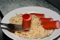 Spaghetti and sausage on a plate. Ketchup on sausages close up