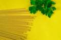 Spaghetti sticks and parsley leaves on yellow kitchen table background. Food photo for recipe, Italian cuisine or restaurant menu Royalty Free Stock Photo