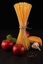 Spaghetti, tomatoes, spices, cheese, basil sprig on a black background