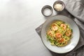 Spaghetti with zucchini courgettes, spring onions and prawns in a grey plate on a white painted table, napkin and small salt and