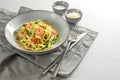 Spaghetti with zucchini courgettes, spring onions and prawns in a grey plate on a white table with a napkin and cutlery, healthy