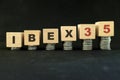 Spain stock market economy growth and recovery concept. IBEX 35 index in wooden blocks with increasing stack of coins in black bac Royalty Free Stock Photo