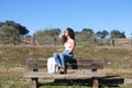 Spanish, brunette, curly-haired woman sits on a bench on the path leading to the forest. She is dressed in jeans and a white top Royalty Free Stock Photo