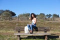 Spanish, brunette, curly-haired woman sits on a bench on the path leading to the forest. She is dressed in jeans and a white top Royalty Free Stock Photo