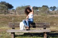 Spanish, brunette, curly-haired woman sits on a bench on the path leading to the forest. She is dressed in jeans and a white top Royalty Free Stock Photo