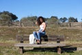 Spanish, brunette, curly-haired woman sits on a bench on the path leading to the forest. She is dressed in jeans and a white top Royalty Free Stock Photo