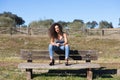 Spanish, brunette, curly-haired woman sits on a bench on the path leading to the forest. She is dressed in jeans and a white top Royalty Free Stock Photo