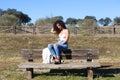 Spanish, brunette, curly-haired woman sits on a bench on the path leading to the forest. She is dressed in jeans and a white top Royalty Free Stock Photo