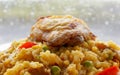 Spanish Paella and Golden Fried Chicken thigh against rainy window background