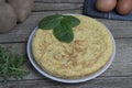 Spanish potato omelette called Tortilla de patatas on a plate, with fresh leaves , eggs and potatoes on wooden rustic background. Royalty Free Stock Photo