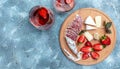 Spanish tapas sliced sausages fuet and Camembert cheese, strawberries and glass rose wine on a wooden cutting board on blue