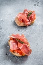 Spanish Tapas with tomatoes and cured Slices of jamon iberico ham, fresh toasts. Gray background. Top view