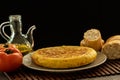 Spanish tortilla, with a glass jar of olive oil and some tomatoes and bread on a dark background Royalty Free Stock Photo