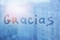 spanish word Gracias are painted on wet blue glass of window on sunset