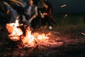 Sparking bonfire with tourist people sit around bright bonfire near camping tent in forest in summer night background. Group of