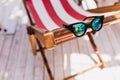 Sparkle female sunglasses lying on striped recliner. Photo of elegant summer glasses on chaise-long