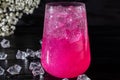 A sparkling brilliant raspberry drink in a glass stands on a wooden table with ice. In the background are roses and a garland Royalty Free Stock Photo