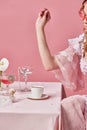Cropped image of charming blond queen, wearing elegant baroque dress sitting at laid table and preparing coffee with