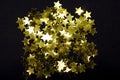 Sparkling and holographic golden star confetti on black background.