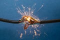 Sparks explosion between electrical cables, on blue background, fire hazard concept, soft focus close up Royalty Free Stock Photo