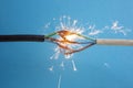Sparks explosion between electrical cables, on blue background, fire hazard concept, soft focus close up Royalty Free Stock Photo