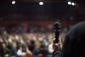 speaker hand with microphone, conference hall with blurred crowd, business corporate event