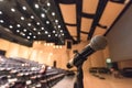 Speaker`s microphone blurred in blurry auditorium music concert hall background or seminar meeting room in educational business