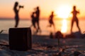 speaker on sand with blurred silhouettes of people dancing by the seaside at sunset Royalty Free Stock Photo