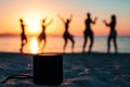 speaker on sand with blurred silhouettes of people dancing by the seaside at sunset Royalty Free Stock Photo