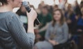 The speaker speaks with a microphone in front of a group of people. Photo is blurry