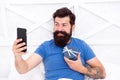 Special gift. Bearded man using mobile technology in bed. Handsome guy taking selfie with gift box. Happy selfie. Modern Royalty Free Stock Photo