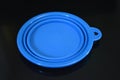 Blue folding and multifunctional rubber plate, a bowl with a plastic edging on a black glossy surface.