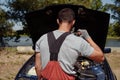 Mechanic standing in front of the open hood and repairing the car