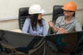 A specialist in a helmet and glasses talks with a female engineer. Technical professionals talk in front of the monitor screens. A