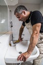 Specialist male plumber repairs faucet in bathroom