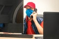 A specialist in a medical mask and a red cap sits between two monitors. The man is talking on the phone in the office during Royalty Free Stock Photo