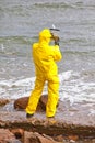 Pecialist in protective suit checking sample of water on rocky sea shore