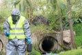 A specialist in a protective suit and mask, is measuring the device, holding it in his hands, on the pond, there is a place for