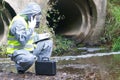 A specialist in a protective suit and mask, on a pond, calls the management on a mobile phone, to report the results of the study